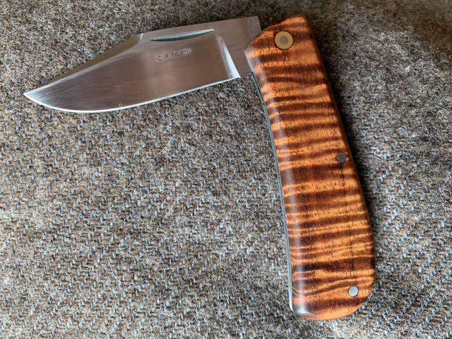 A folding knife with a wood treated handle on a grey and brown carpet.