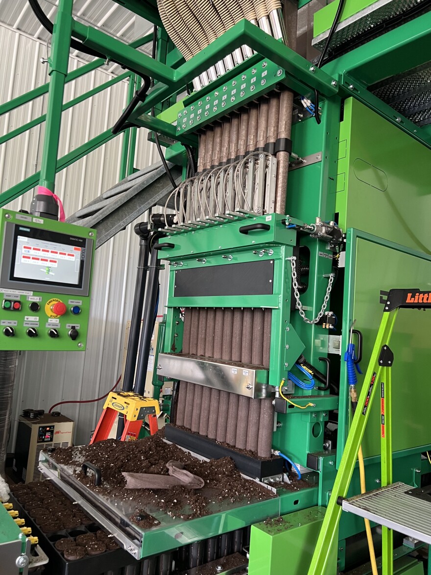 A big green machine wraps cylinders of soil in biodegradable paper.
