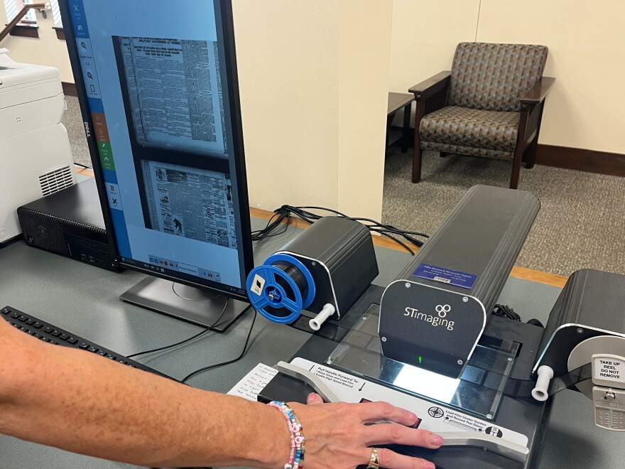 PPL Assistant Director AnnDee Peterson demonstrates how to use the microfilm machine. A reel with scans of old newspaper pages is being run through the machine, and the scans are being displayed on a computer monitor.