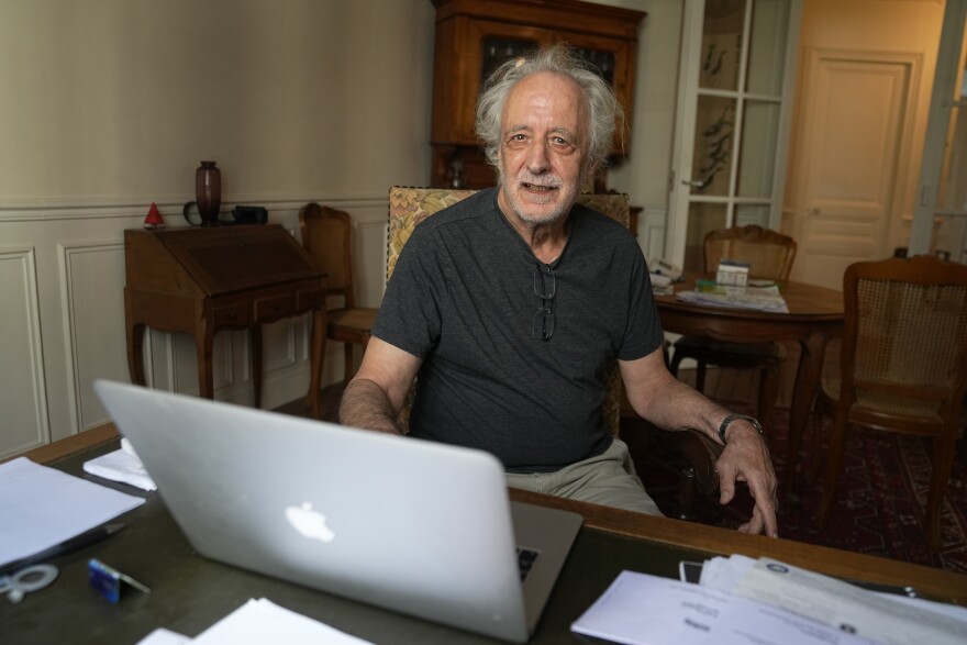 French scientist Pierre Agostini poses in his apartment at a desk with his laptop.
