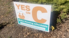 A sign standing in dirt reads "Yes on C. Make housing affordable." 