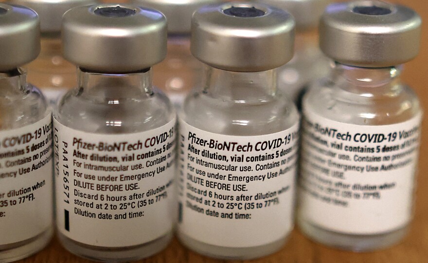 A close-up of four small, clear vials labeled "Pfizer-BioNTech COVID-19 vaccine."