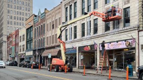 Buildings line a street in downtown Steubenville in eastern Ohio. A person on an orange lift works on one of the facades. 