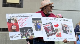 A man stands outside the jail holding two signs that include photos and the words #justice4christianblack and #stand4christian
