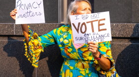 A protester holds up anti-Flock placades outside Richmond City Hall during a demonstration against Flock cameras before a City Council meeting on July 27, 2026.