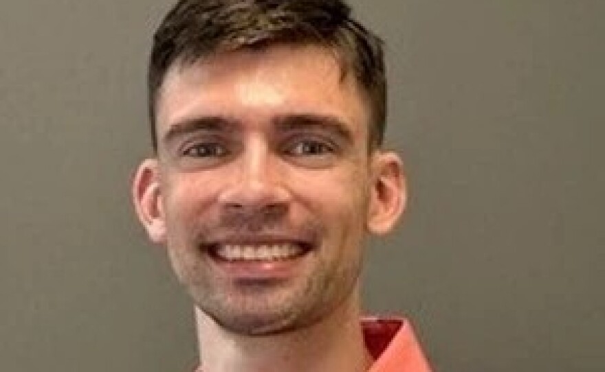 A smiling man with short brown hair wears a salmon colored button-down shirt.
