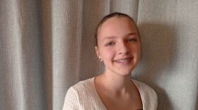 Sydnee May, a middle-schooler, stands in front of a curtain, smiling.