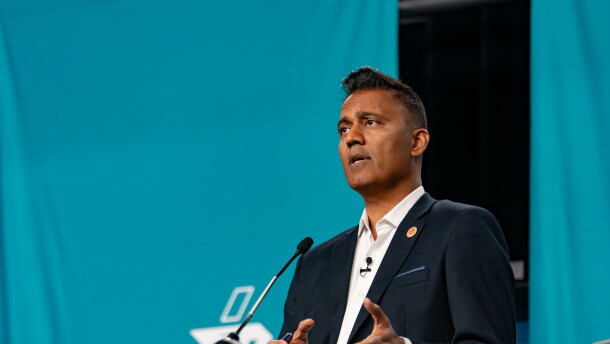 Man with short dark hair and black suit speaks behind podium