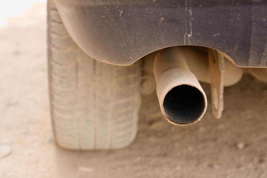  A close-up of a car's tailpipe. The car is dusty on a gravel road. 
