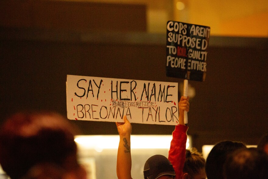 Photo of protesters holdings signs that read "Say her name, Breonna Taylor, Black Lives Matter" and "Cops aren't supposed to kill guilty people either."