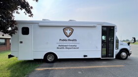 A white bus with Ashland County's public health logo is parked in a lot.