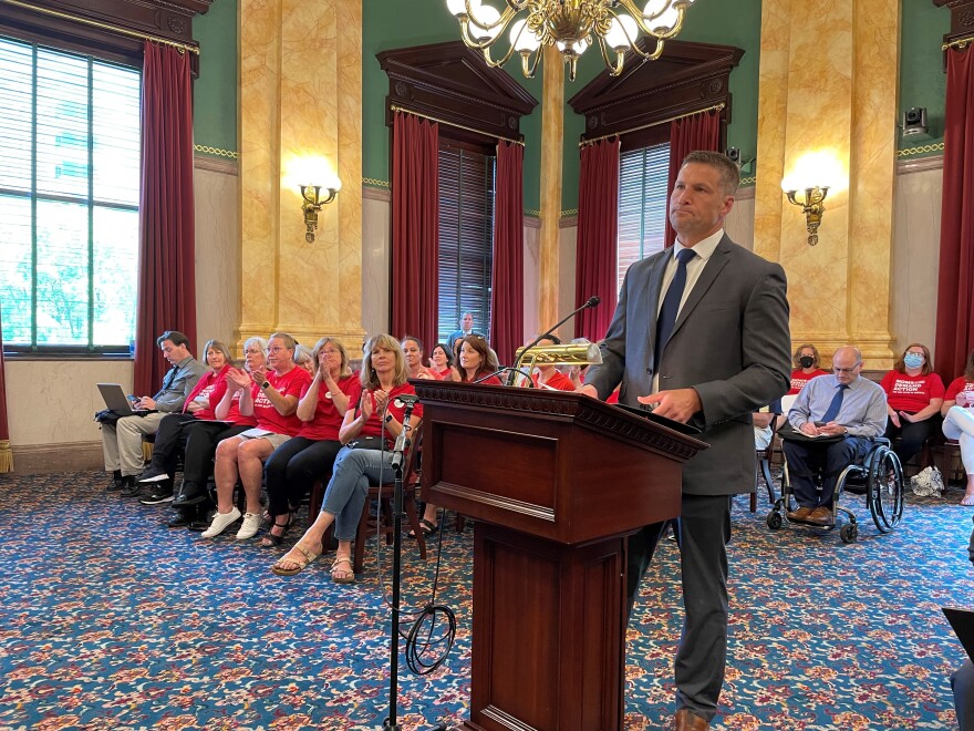 Ben Adams gets applause from House Bill 99 opponents as he testifies against the bill in a Senate committee on May 31, 2022. He was among the parents who sued the Madison Local School District over armed personnel training requirements. The Ohio Supreme Court agreed with the parents, ruling the district had to require more than 700 hours of training. That decision led the son of the district's school resource officer, Rep. Thomas Hall (R-Middletown), to draft House Bill 99. [Karen Kasler /  Statehouse News Bureau]