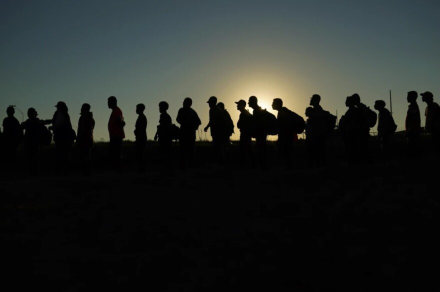 A line of people are seen in shadow as the sun sets behind them.