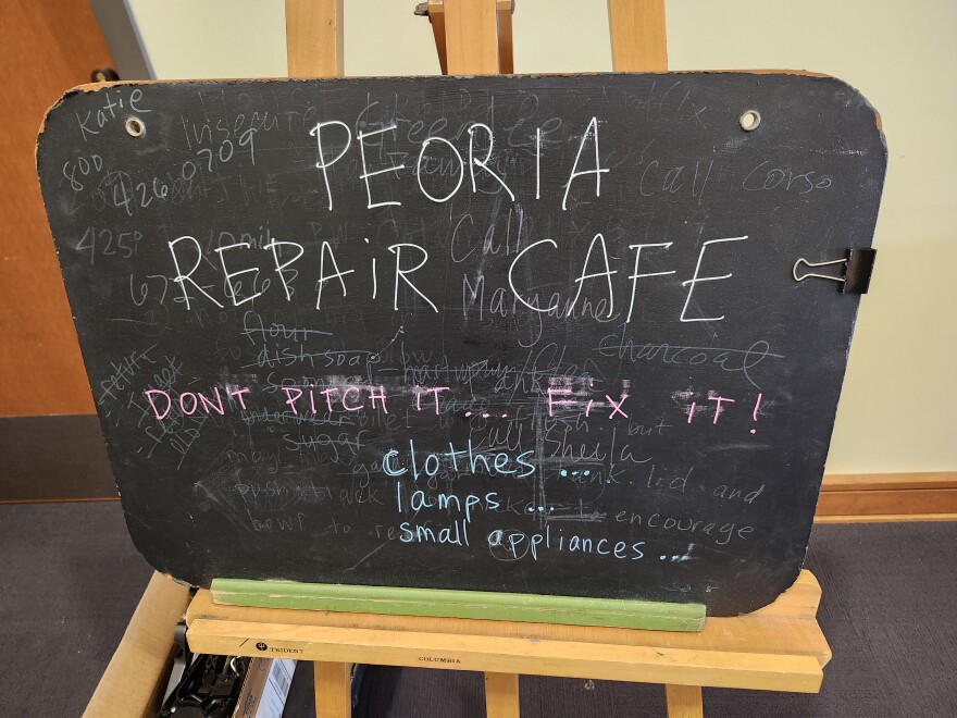 A blackboard that reads "Peoria Repair Cafe. Don't pitch it...Fix it! Clothes, lamps, small appliances."