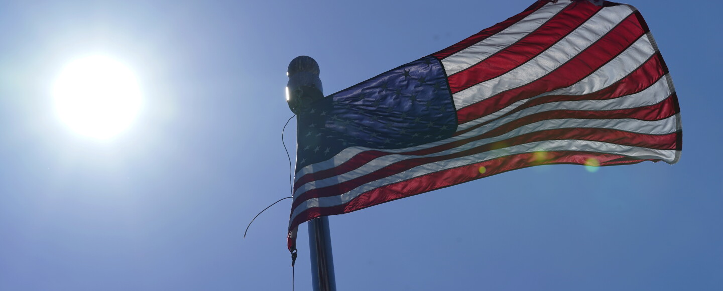 A U.S. flag flies with the sun in the background.