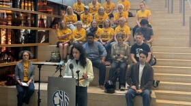 A group of activists stand behind a podium for a press conference on the steps inside Seattle City Hall. 