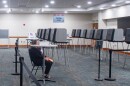About a dozen voting machines set up in a large conference room. One poll worker sits to greet voters.