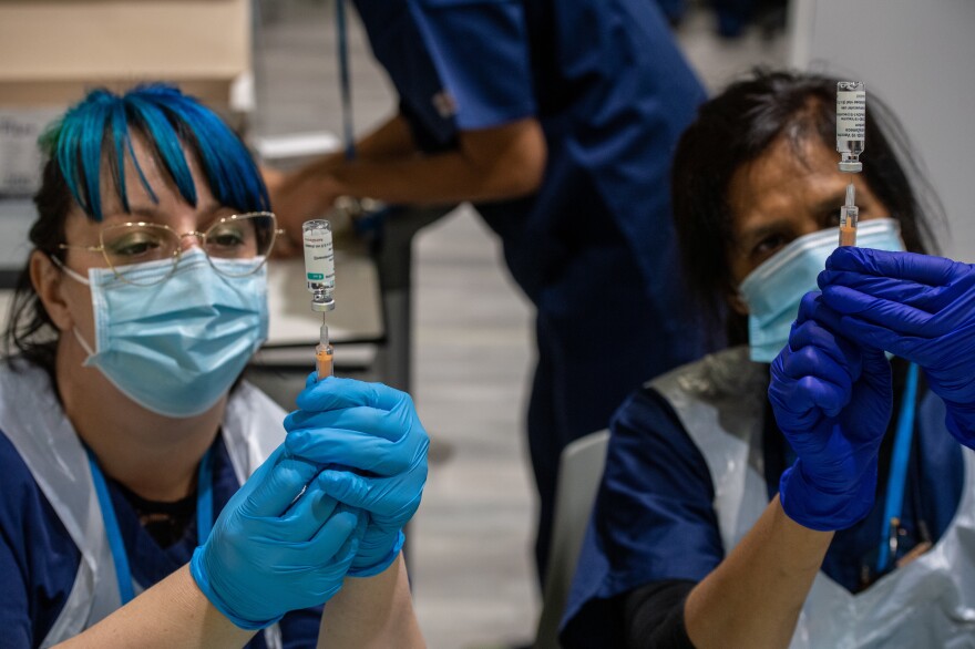 Two health care workers prepare syringes with AstraZeneca's COVID-19 vaccine in London Monday. A U.K. study will expose volunteers to the coronavirus and could help development of future vaccines.
