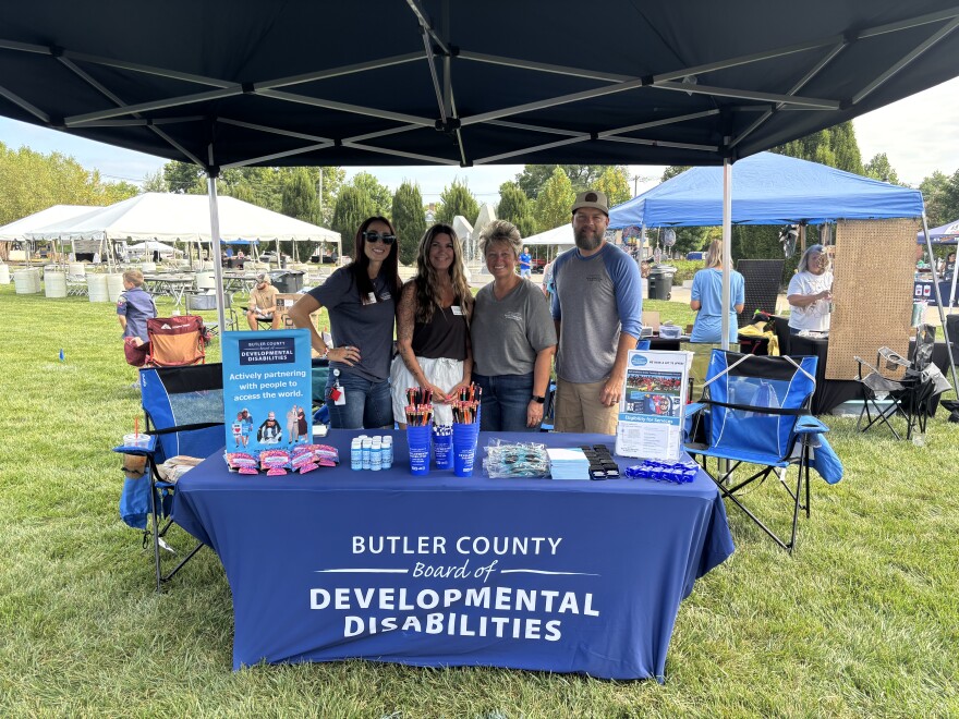 four people stand around an event table smiling at the camera