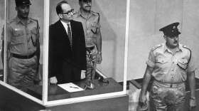 Adolf Eichmann stands in his bullet-proof glass cage in Israel's Supreme Court.