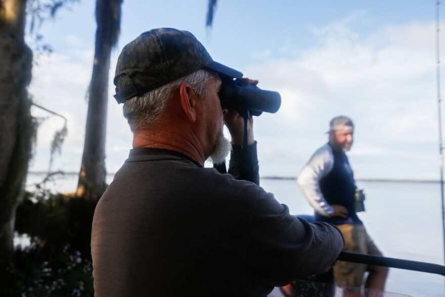 Richie Smith looks through binoculars after Alex Horton moved the boat near the shoreline in search of alligators on October 26, 2019. (Chris Day/Fresh Take Florida)