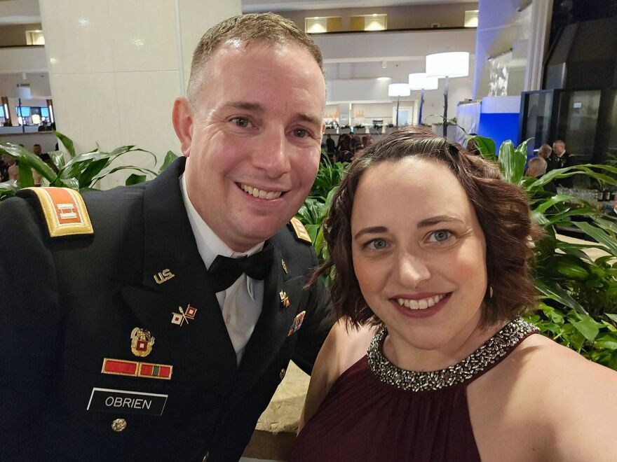 A man in a black, military dress uniform takes a selfie with a woman wearing a black evening gown.