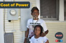 An older Black man with a gray goatee standing on the side of a yellow house, with his left hand on a young girl's shoulder. They're standing in front of a power meter on the house. A grey and yellow text saying "The Cost of Power" to the left 