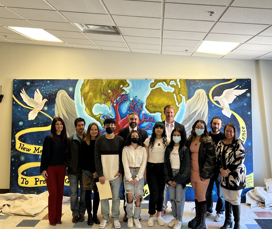 Students, staff, and elected officials gather in front of the mural