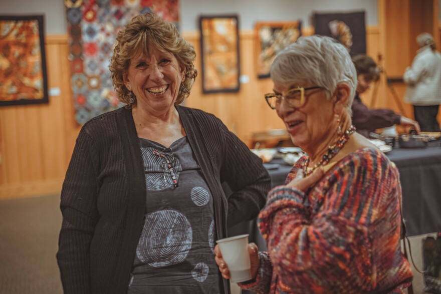 two women stand laughing and smiling in an art gallery