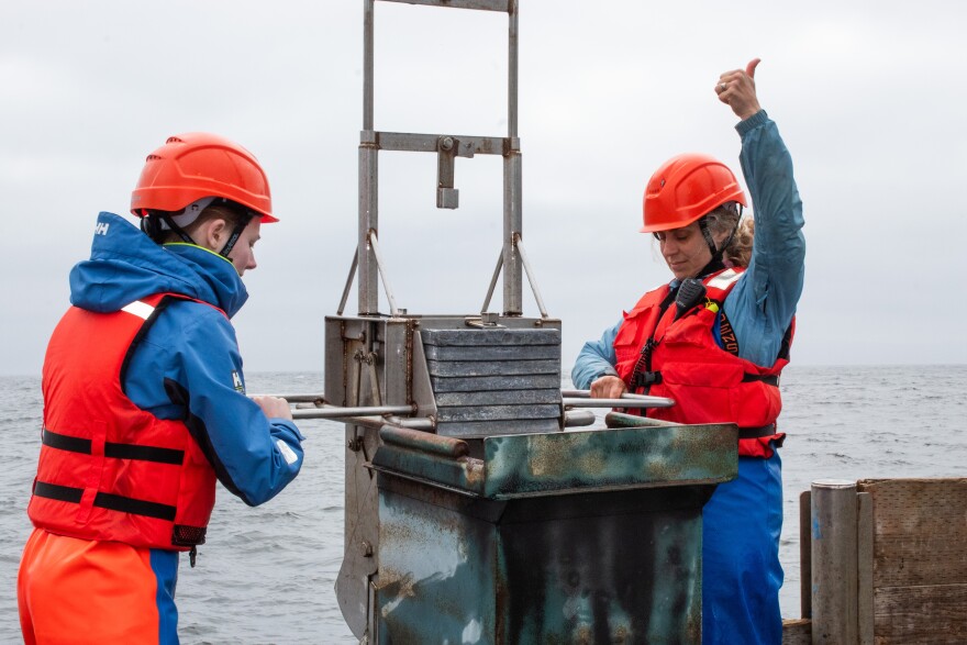 Two people lift a device out of the ocean water on the deck of a boat.