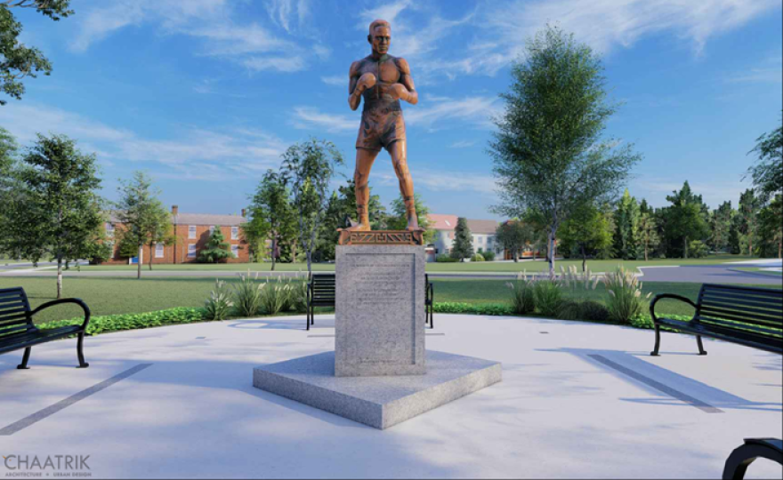 artistic rendering of bronze statue of man in boxing stance atop a stone pedestal surrounded by a concrete oval with benches and trees in the background.