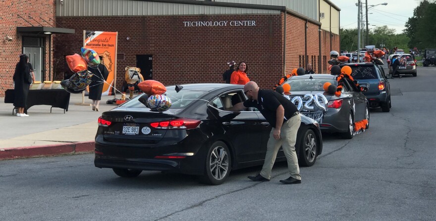 A staff member reaches into a vehicle to deliver a diploma at Martinsburg High School’s drive-through graduation on May 26, 2020. The majority of faculty and staff did not wear protective equipment or follow social distancing guidelines to combat the coro