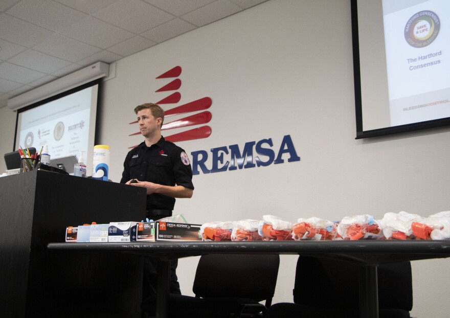 A paramedic stands in front of a podium and table. Behind him the REMSA logo can be seen.