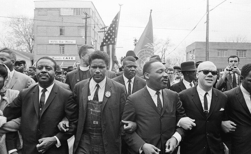 Dr. Martin Luther King, Jr. locks arms with his aides as he leads a march of several thousands to the court house in Montgomery, Ala., March 17, 1965. From left: Rev. Ralph Abernathy, James Foreman, King, Jesse Douglas, Sr., and John Lewis (partially out 