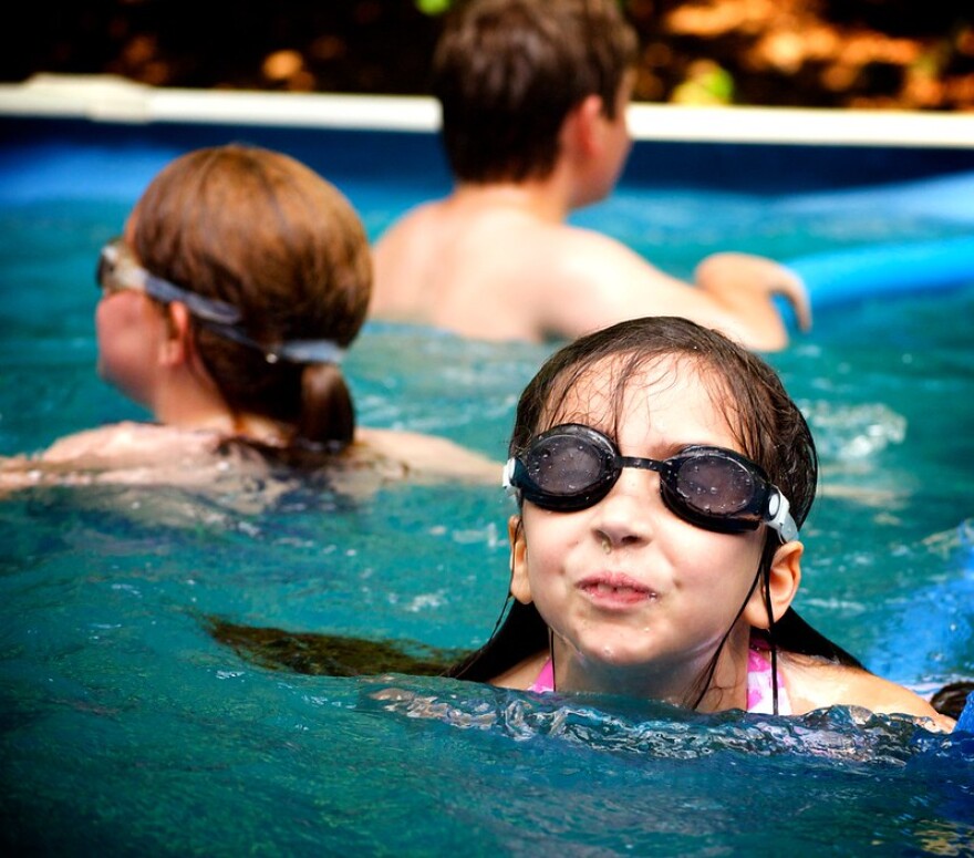 Children play in a pool. One child looks like she is going to spit water out of her mouth at the camera.