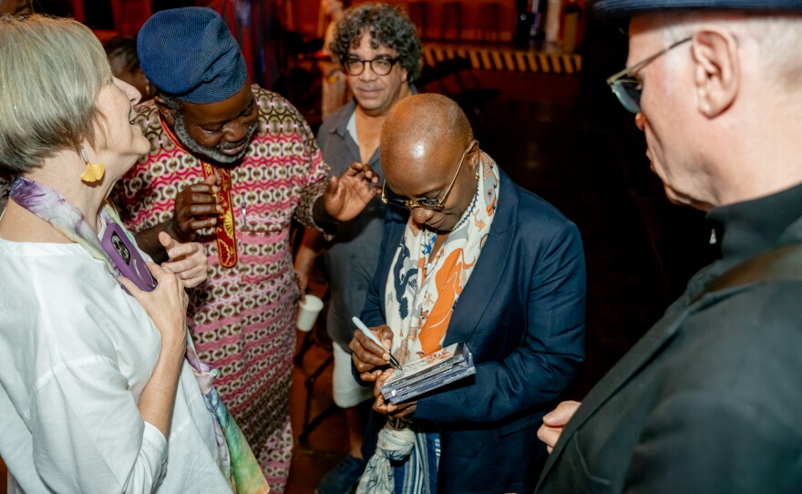 Grammy winner Angélique Kidjo stands in a circle of fans and signs a stack of CDs after her interview with "African Perspectives" host Akinloyè Òjó