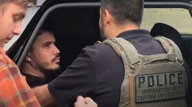 Immigration and Customs Enforcement police officer confronting man in back of police vehicle.