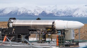A sleek, silver rocket - called Astra's One of Three - sits in front of snow-covered mountains.