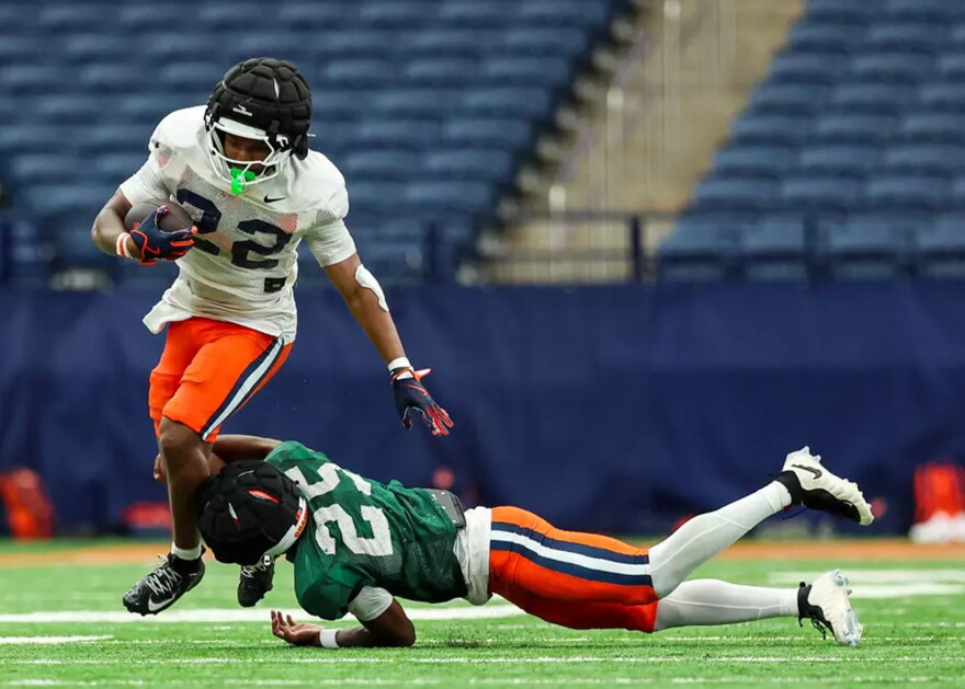 Running back Ahmad Miller (22, white) breaks a tackle from defensive back Cam Hairston-Taylor (25, green) in Syracuse’s offseason scrimmage.