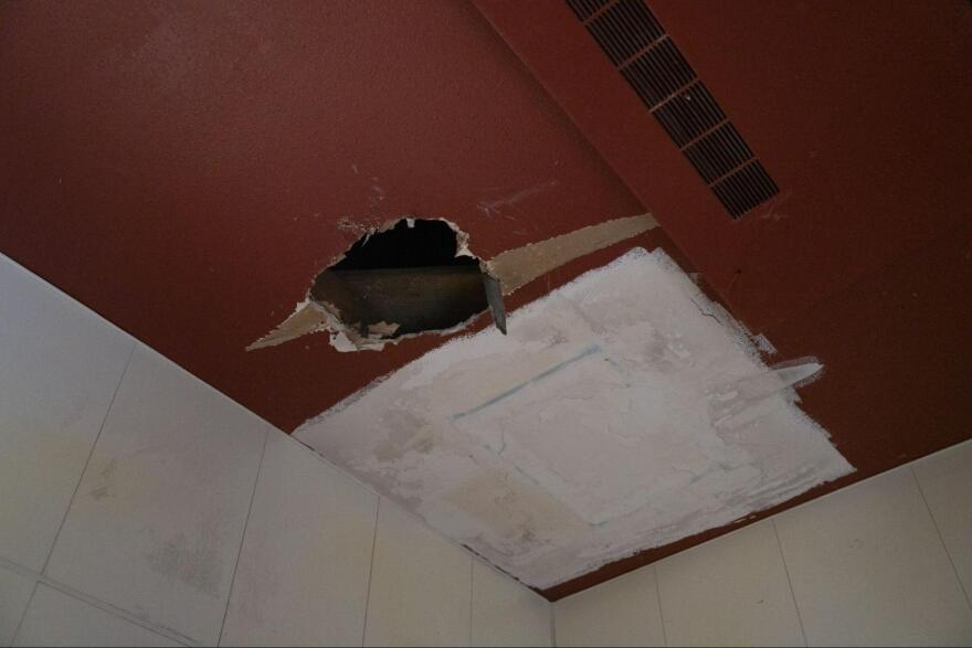 A large hole in a ceiling with paint peeling around it.