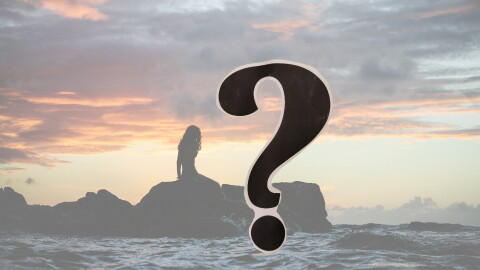 Silhouette of a woman on a line of rocks in the ocean at sunset; a question mark in the foreground 