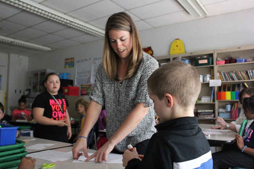 A teacher points to a paper on a student's desk