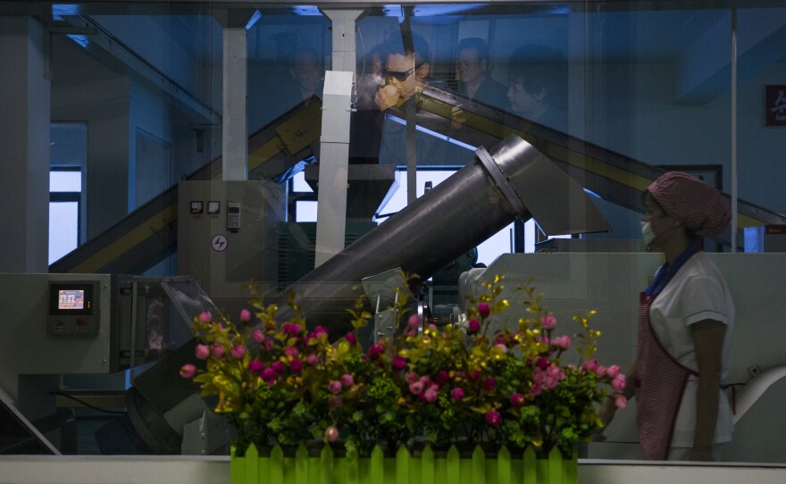 Behind the glass, a worker at a cosmetics factory in Pyongyang. A photograph of Kim Jong Il that commemorates a visit to the factory is seen in the reflection.