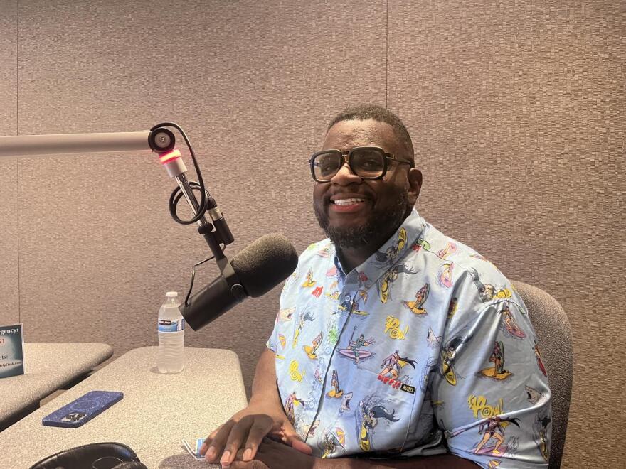 Man holds KJZZ sign while sitting in front of microphone in recording studio