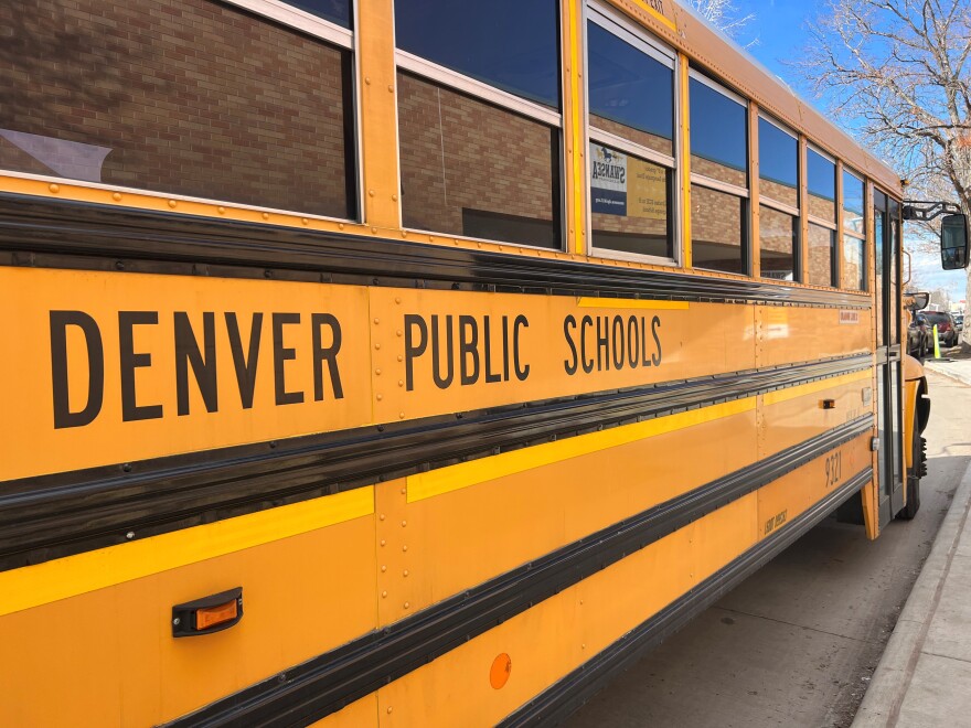 A yellow school bus is parked by a curb. The sign on the bus says "Denver Public Schools."