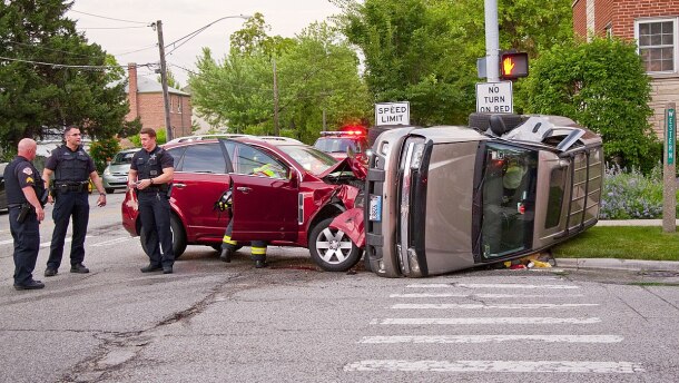 Three police officers standing next to a crash involving two cars, one of which is on its side.  