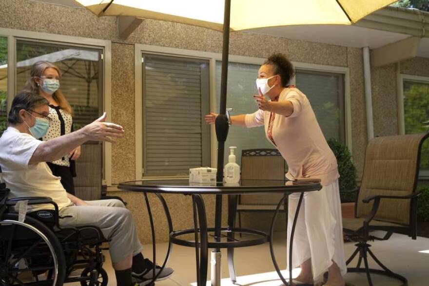 Deborah Trigueiro, right, greets her husband Douglas Smith, with a big hug from across the table at the Life Care Center of Kirkland on August 24, 2020, in Kirkland, Washington. This is only the second time they have seen each other in person since February when the coronavirus (COVID-19) raced through the facility.