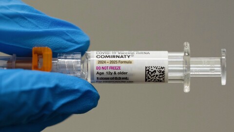 Close-up view of blue-gloved fingers holding syringe with "Comirnaty" label