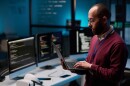 Side view portrait of bearded adult man as computer programmer holding open laptop in IT and cybersecurity office with blue lights copy space