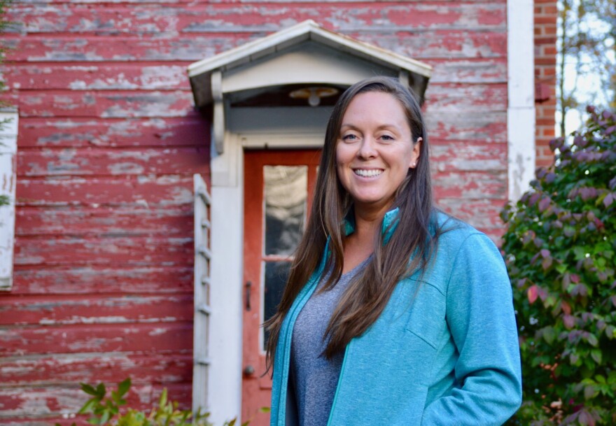 Amanda O'Connor wears a blue jacket and stands in front of a red building with a red door.